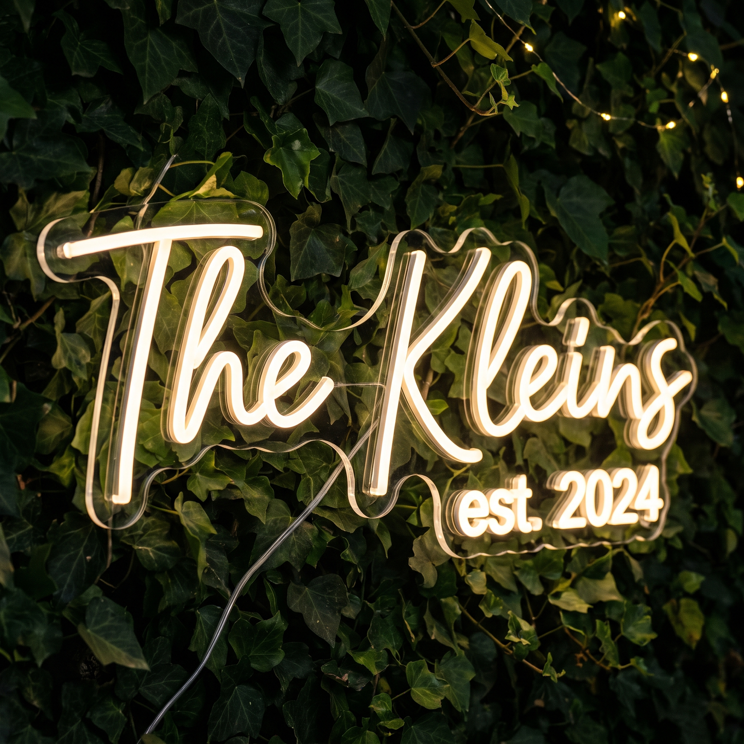 LED-Neonschild „The Kleins“ an einer Efeuwand in Nahaufnahme – Neon Atelier