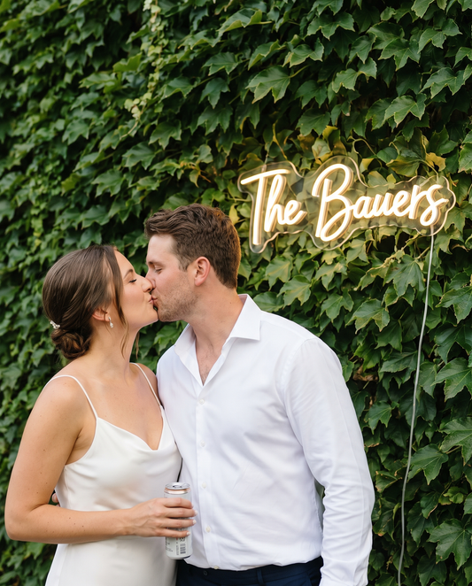 LED-Neonschild „The Bauers“ an einer Efeuwand, küssendes Brautpaar – Neon Atelier